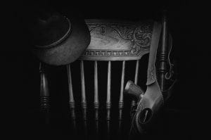 Black and white photo of holster and hat hanging over chair